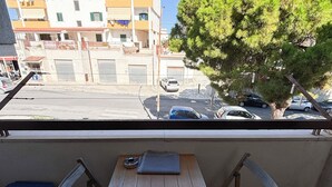 Un balcón con una mesa de madera y dos sillas, con vistas a una calle con coches aparcados y edificios.