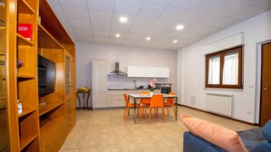 Eine moderne Küche mit weißen Schränken, einem Esstisch mit orangefarbenen Stühlen und einem blauen Sofa mit einem pfirsichfarbenen Kissen.