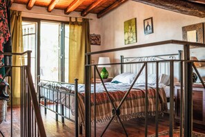 A bedroom with a metal bed frame, wooden flooring, a green curtain, and a window with a view. - Vigna Dell'Etna (Piedimonte Etneo)