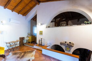 A spacious living area with a wooden ceiling, a fireplace, and a dining area with a yellow chair and a table. - Vigna Dell'Etna (Piedimonte Etneo)