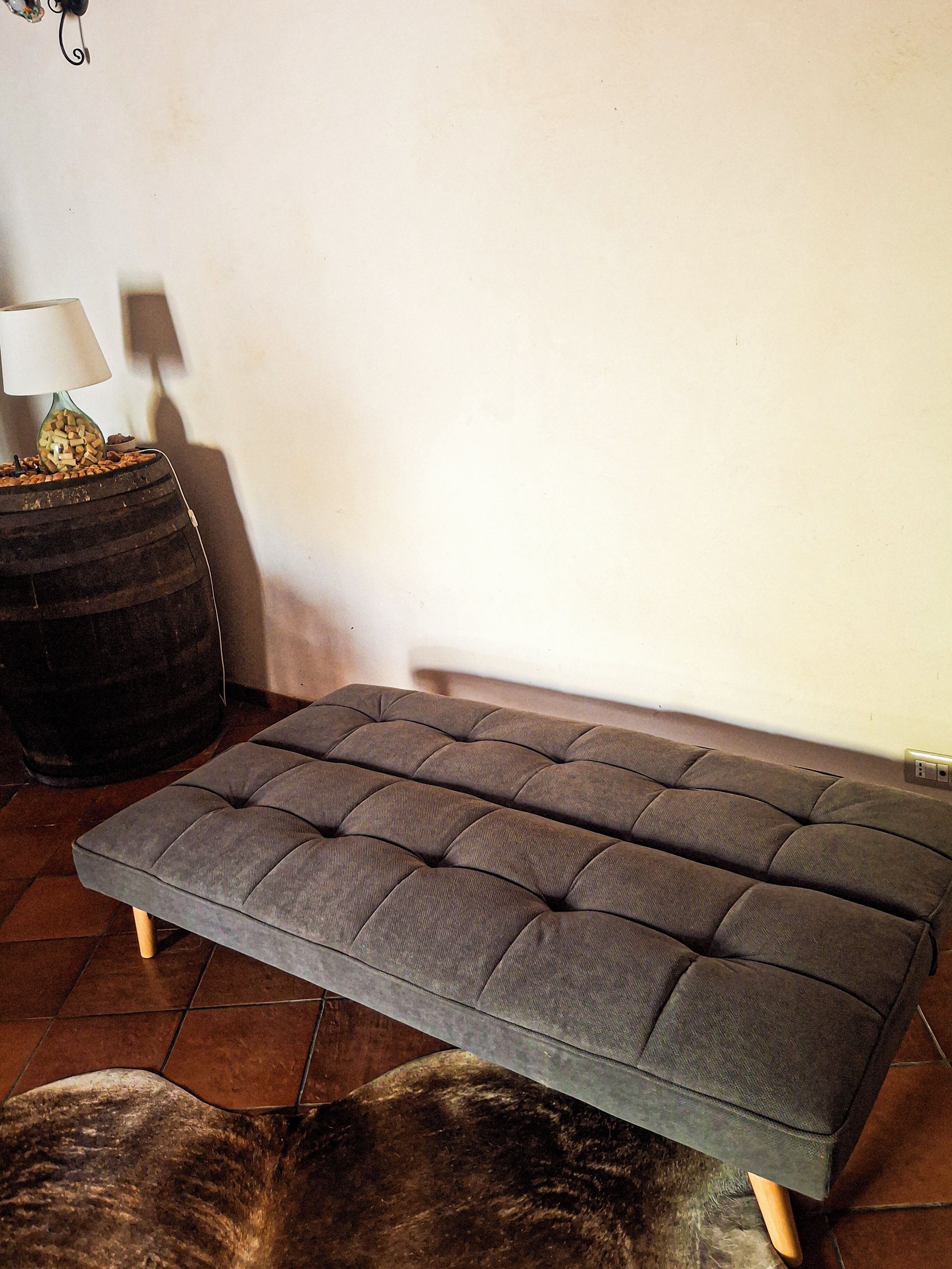 Una habitación con un sofá tapizado gris, una mesa redonda negra con una lámpara, y una alfombra de piel en el suelo.