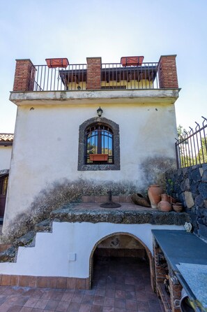 A building with a balcony, a window with a decorative frame, and a stone wall. - Vigna Dell'Etna (Piedimonte Etneo)