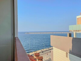 Vista da un balcone su una zona costiera con cielo sereno, spiaggia di sabbia e mare calmo.