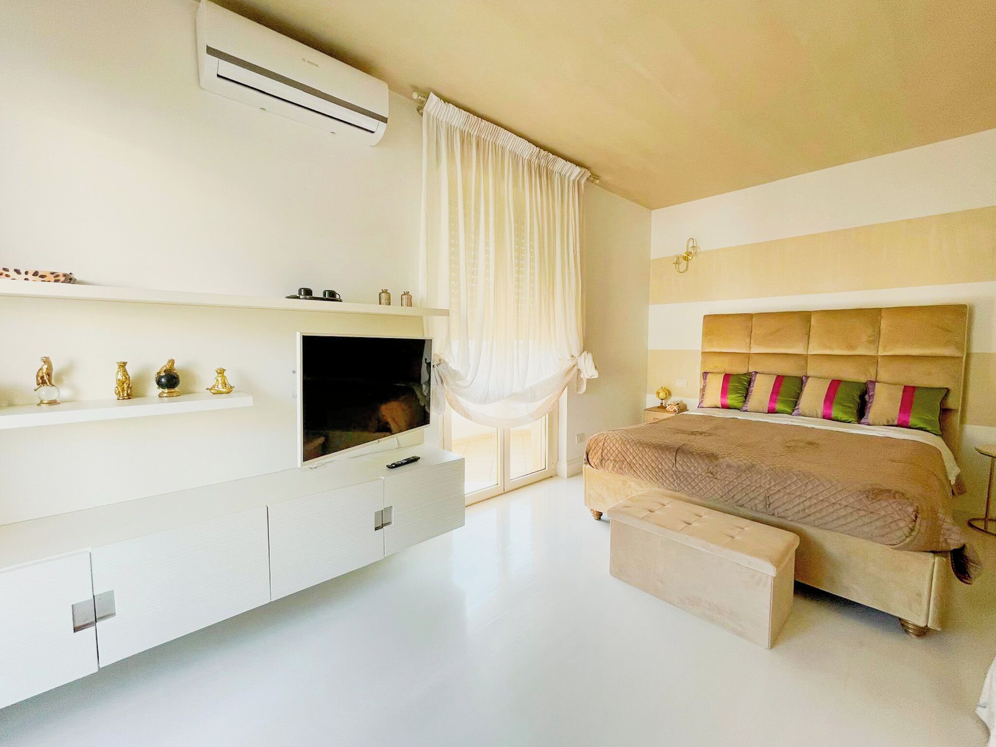 A bedroom with a bed, a TV, a shelf with decorative items, and an air conditioning unit.