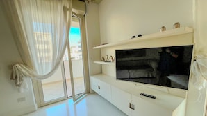 A living room with a large flat-screen TV, white furniture, and a view through a glass door. - Mora Suite (Bari)