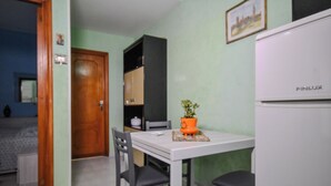 A compact kitchen with a white refrigerator, a dining table with two chairs, and a potted plant on the table. - Casa Ida (San Giovanni Rotondo)