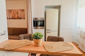 Eine moderne Küche mit Einbauofen, Kühlschrank und Essbereich mit Holztisch und gewebten Untersetzern.