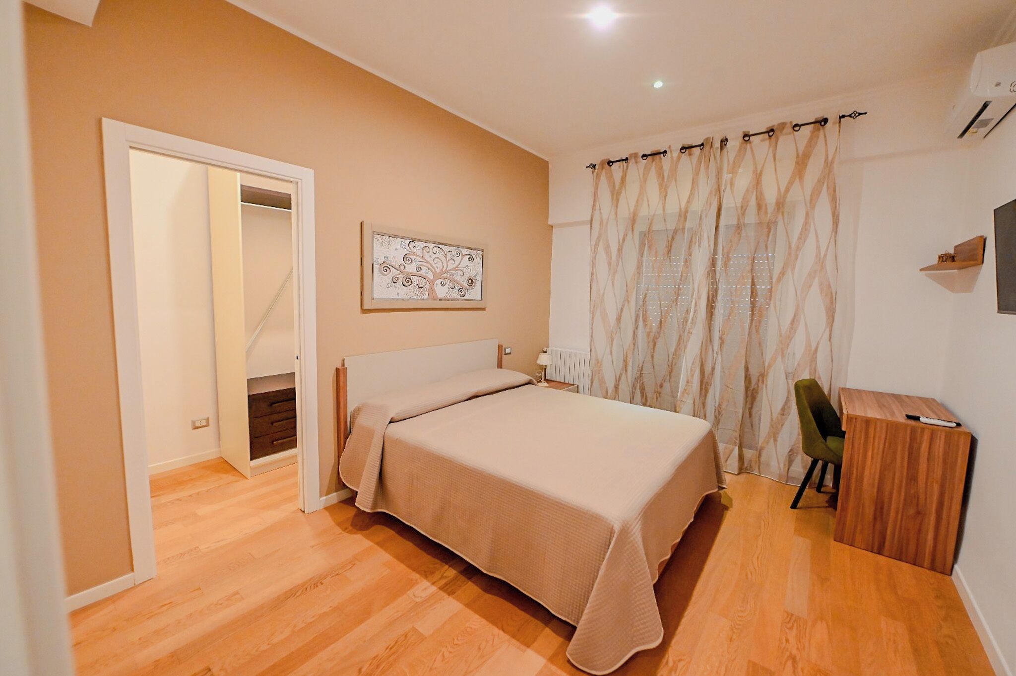A bedroom with a bed, a desk, a chair, a wardrobe, and a window with curtains.