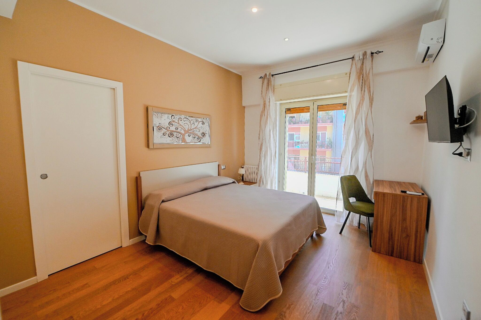 Ein Schlafzimmer mit Bett, Stuhl, Schreibtisch, Gemälde und Fernseher.