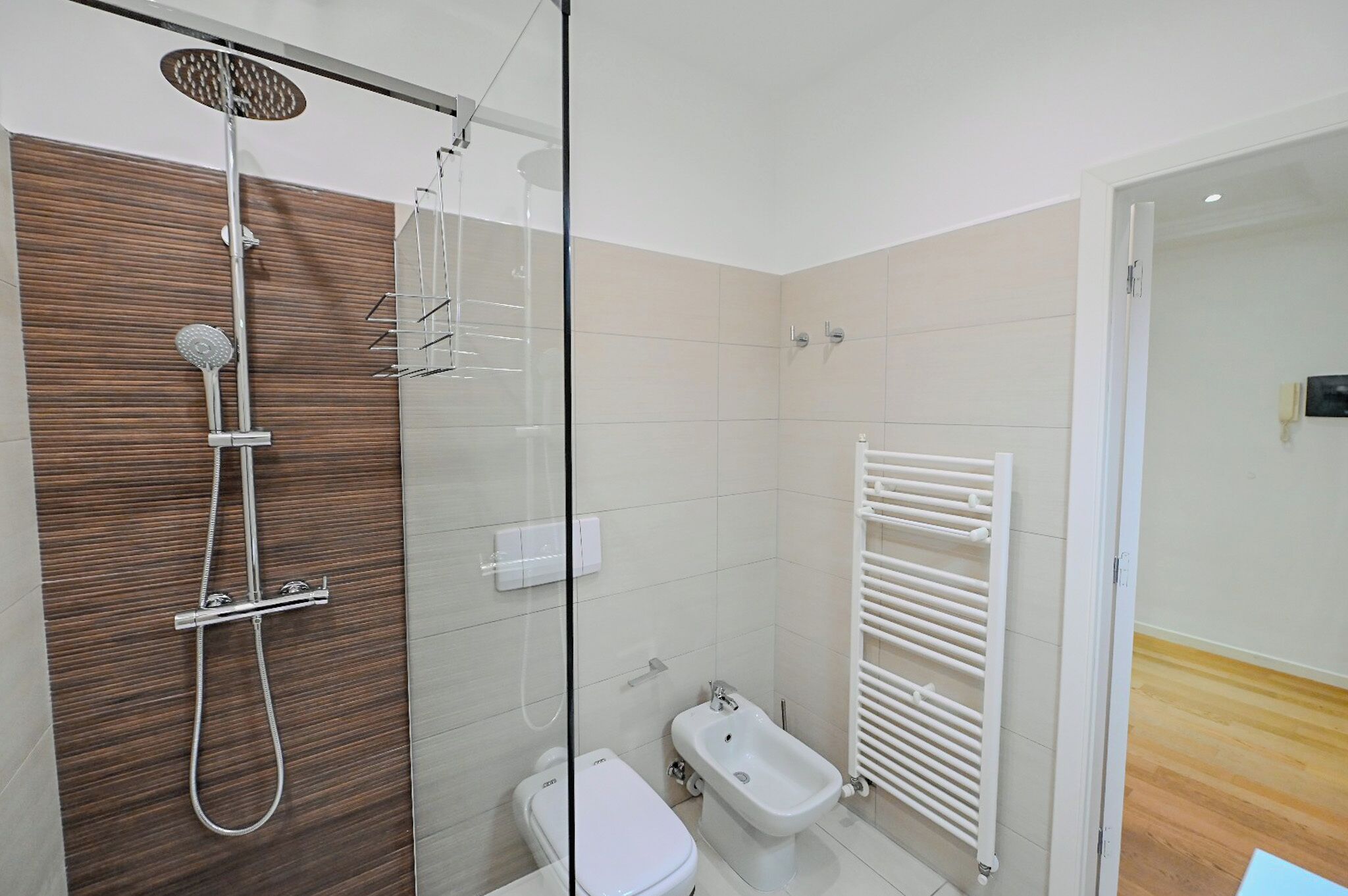 Un baño moderno con ducha acristalada, un bidé y un radiador blanco.