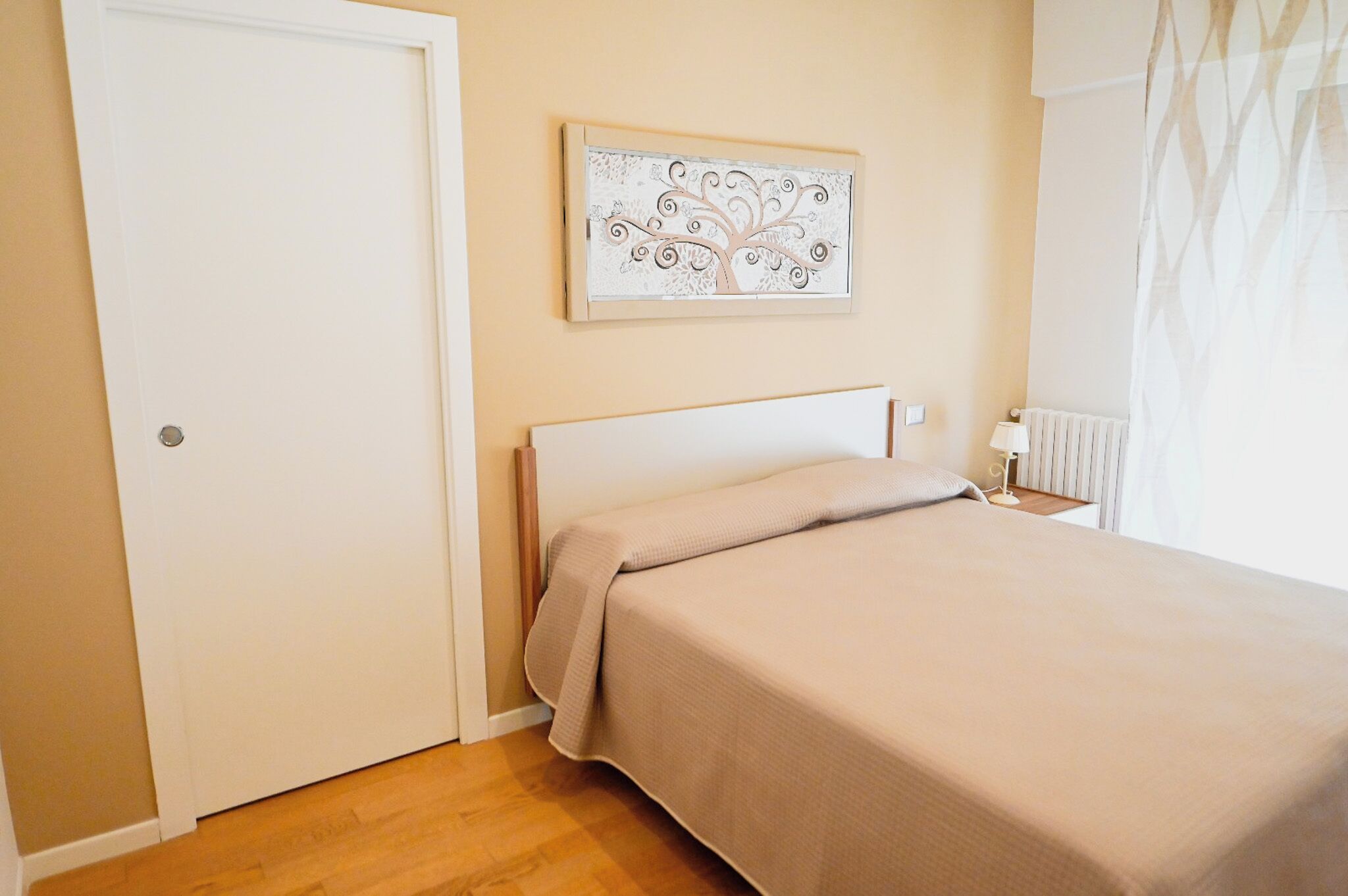 A bedroom with a bed, a nightstand, a wall-mounted lamp, and a door.
