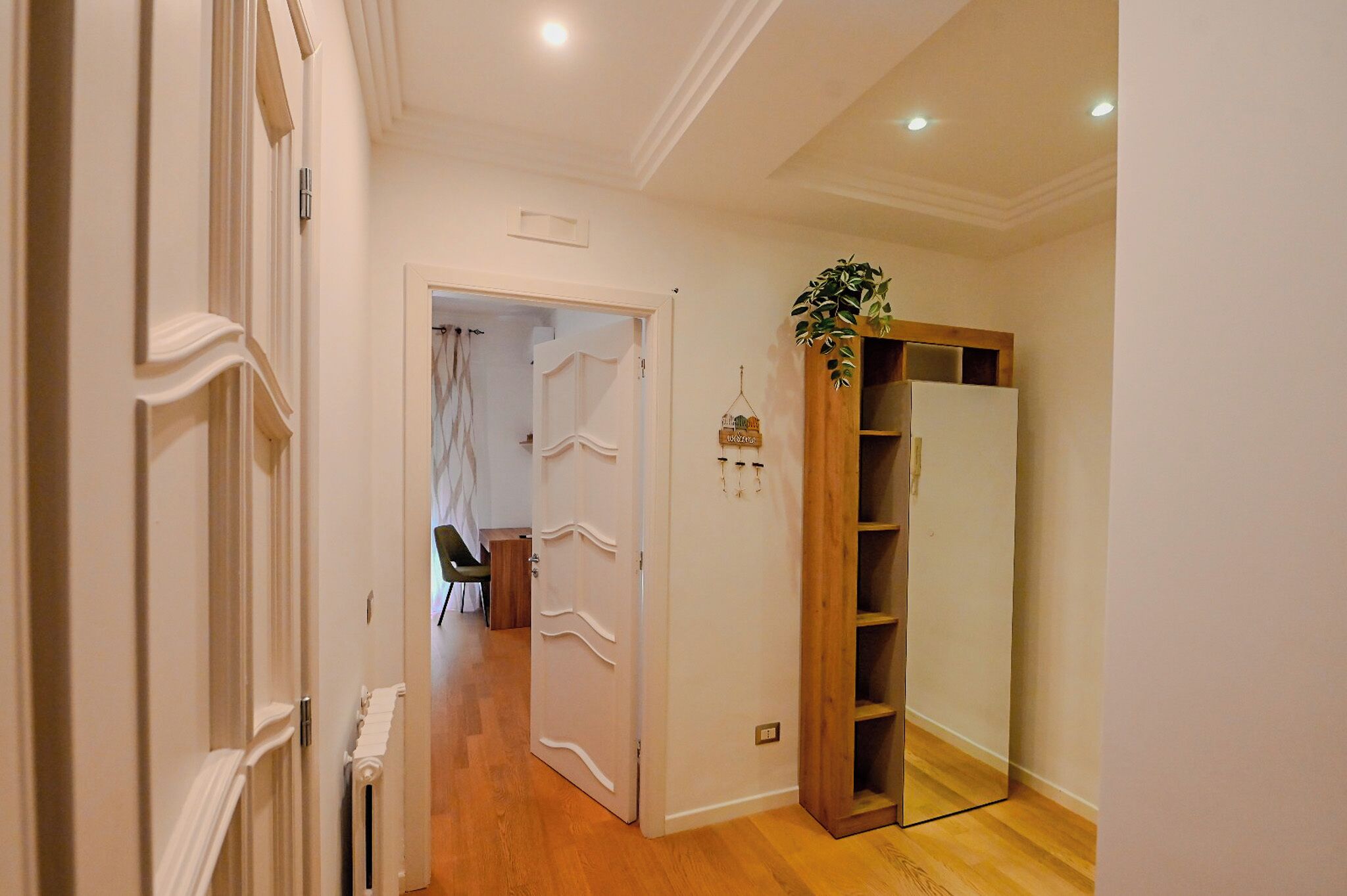A hallway with a white door, a wooden cabinet, and a radiator.