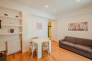 Ein modernes Wohnzimmer mit einem weißen Esstisch, einem braunen Sofa und Kunstwerken an den Wänden.