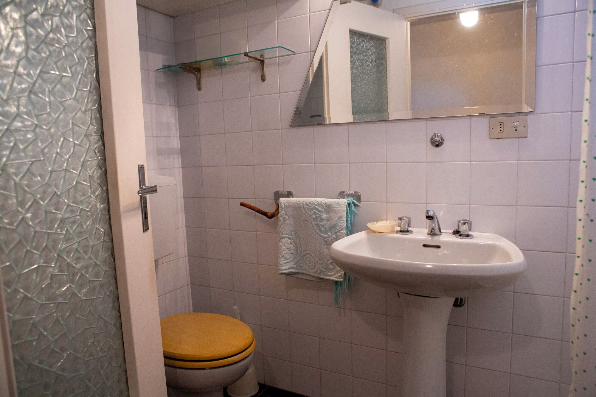 A bathroom with a white sink, a toilet with a wooden seat, and a glass shower enclosure.