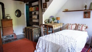 Ein gemütliches Schlafzimmer mit einem Bett, einer Holzkommode, einem Bücherregal und einem Schreibtisch mit einer Lampe.