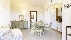 Zona pranzo con tavolo rotondo e sedie, angolo cottura con mobili ed elettrodomestici, e un letto con cappello e coperta.