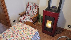 Um quarto aconchegante com uma cadeira de madeira coberta por um cobertor estampado, um aquecedor pequeno e uma mesa com toalha colorida.