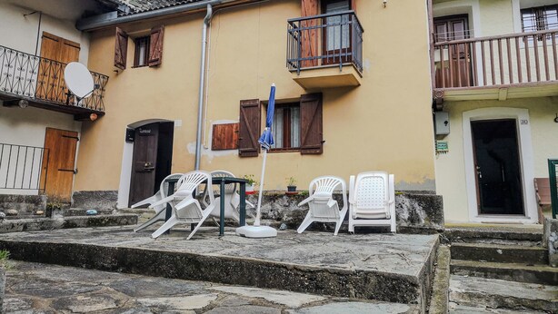 Um edifício com escadaria de pedra que leva a uma porta de madeira, cadeiras de plástico branco e uma antena parabólica na varanda.