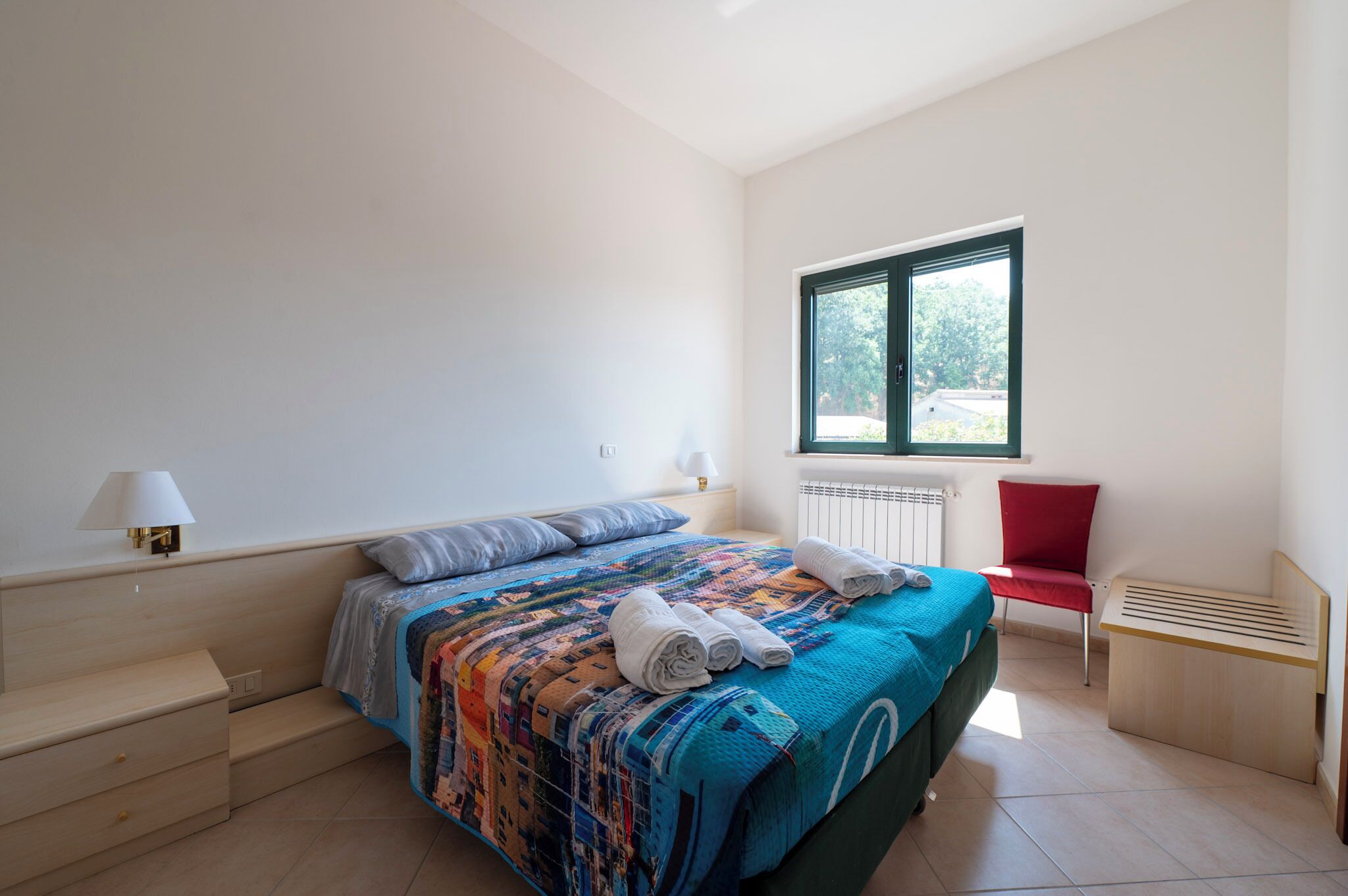 A bedroom with a bed, a chair, a lamp, and a window.