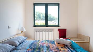 A bedroom with a bed, a window, a radiator, a nightstand, and a wooden bench.