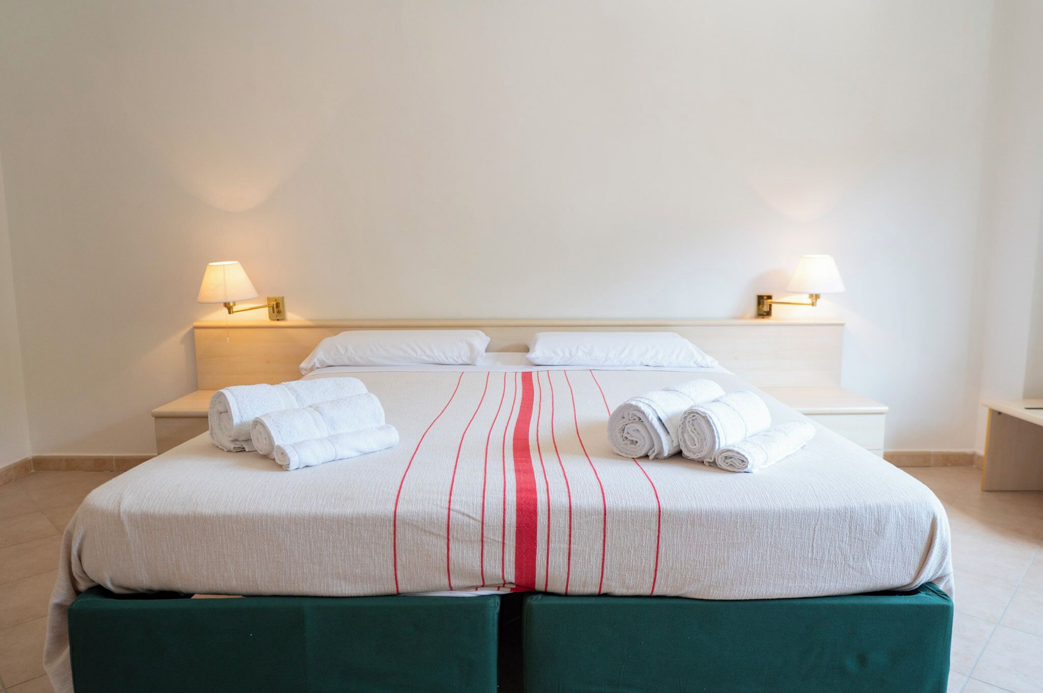 Un lit bien fait, avec du linge de lit blanc à rayures rouges, deux lampes de chevet et une décoration de chambre épurée et minimaliste.