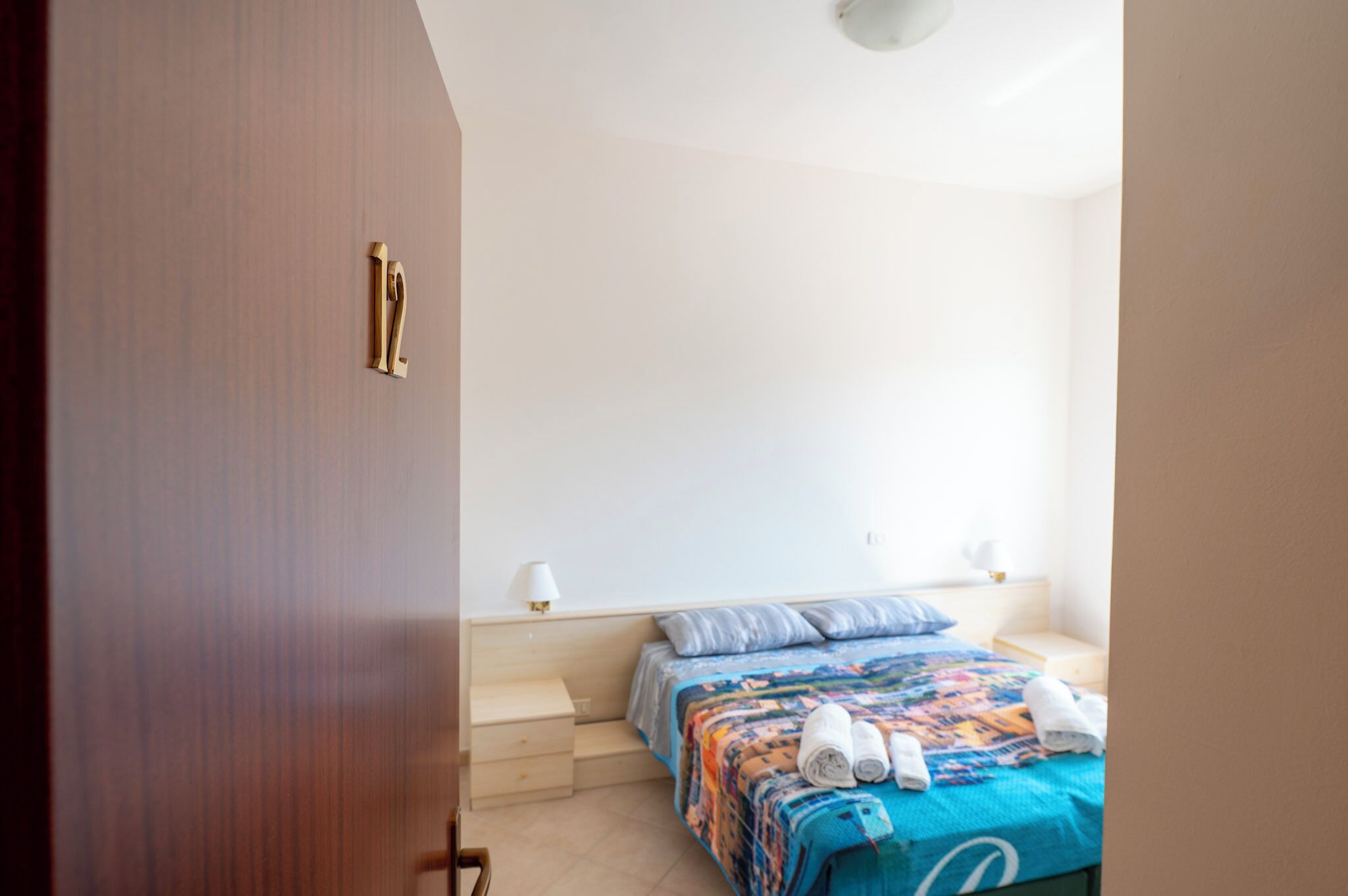A bedroom with a bed, a nightstand, a lamp, and a wooden door.