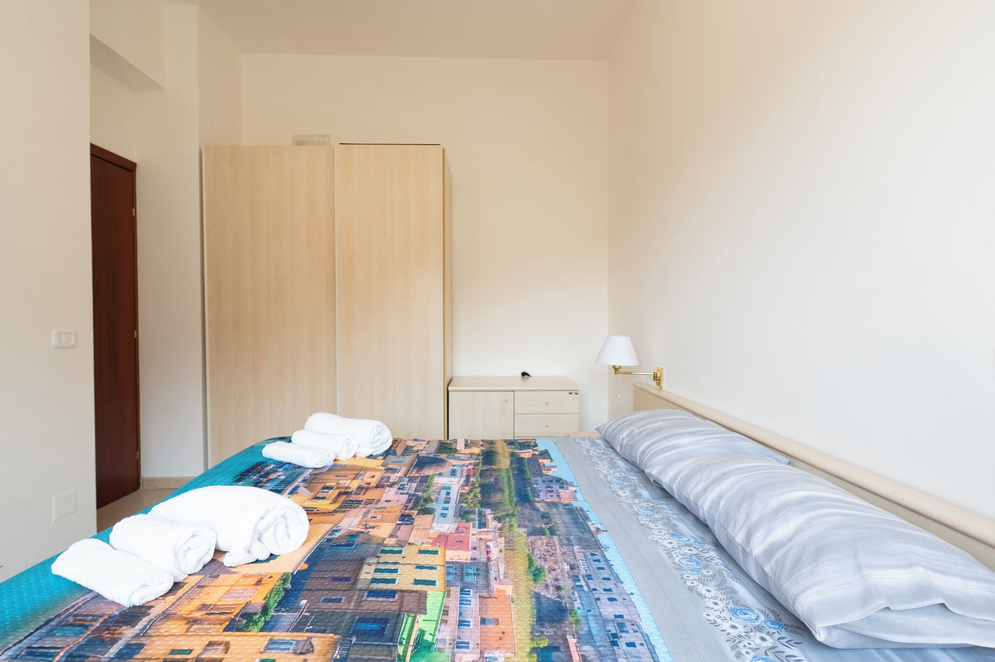 A hotel room with a bed, a nightstand, a lamp, and a wardrobe.
