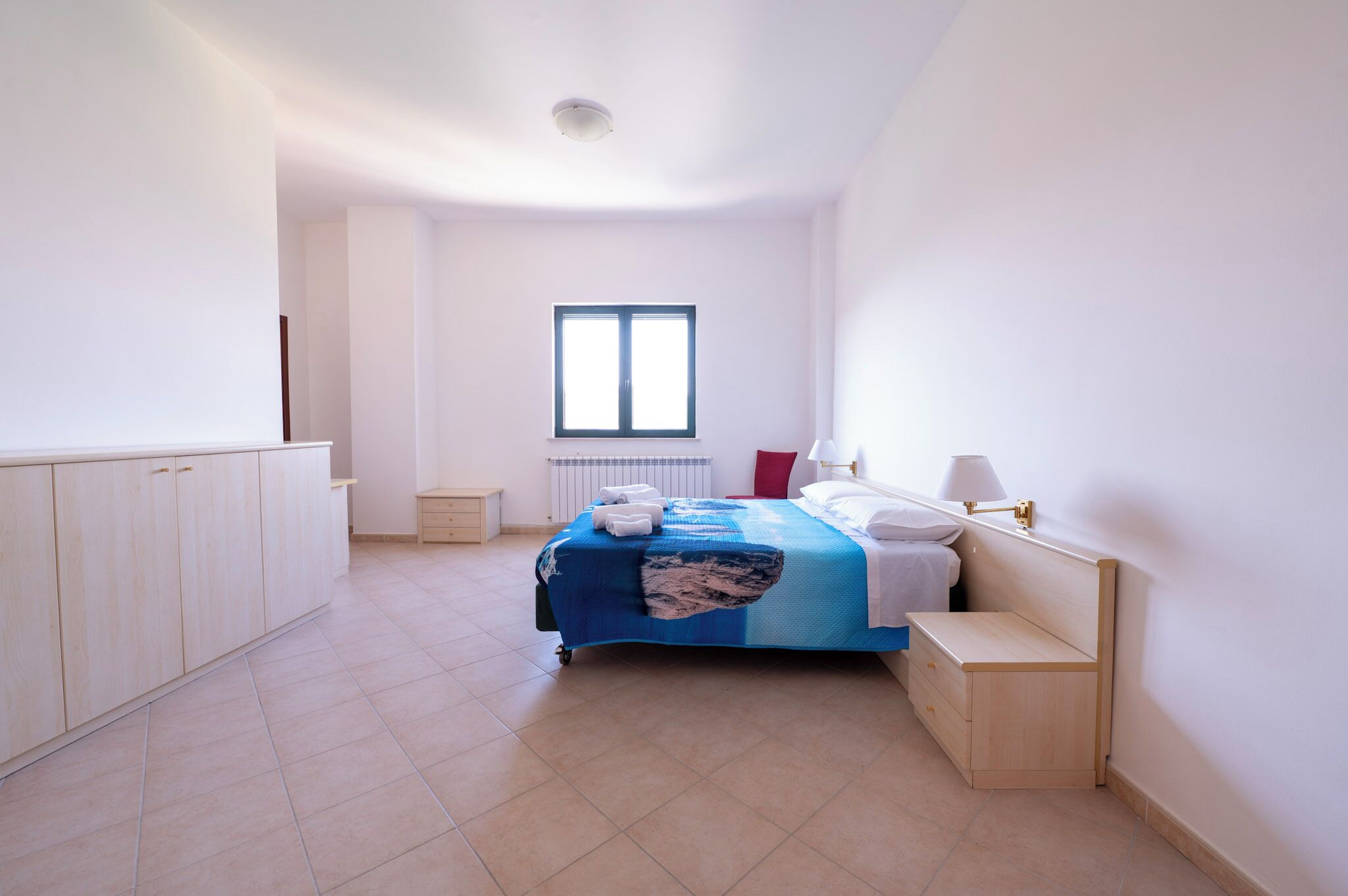 A bedroom with a bed, bedside tables, a window, and a radiator.
