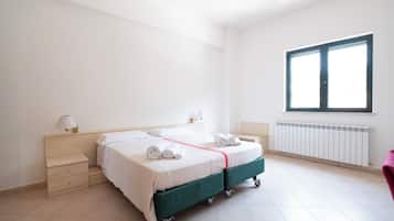 A hotel room with a double bed, a nightstand, a lamp, a window, and a radiator.