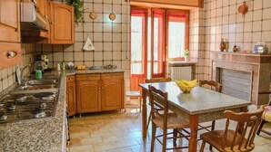 A kitchen with granite countertops, wooden cabinets, a dining table with chairs, and a window with red curtains. - Le Sciosce (San Giorgio Lucano)