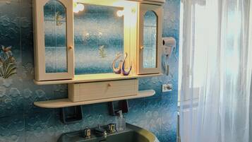 A bathroom with a vanity mirror, a sink, and a hairdryer on a wall.