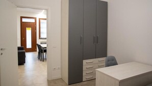 A room with a large grey wardrobe, a desk, and a dining area with chairs and a table. - Sonech (Sonico)