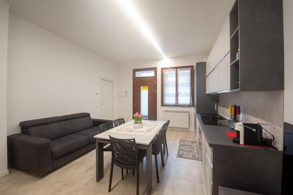 A modern living room with a sofa, dining table, and chairs. There is a kitchen area with cabinets and a countertop.