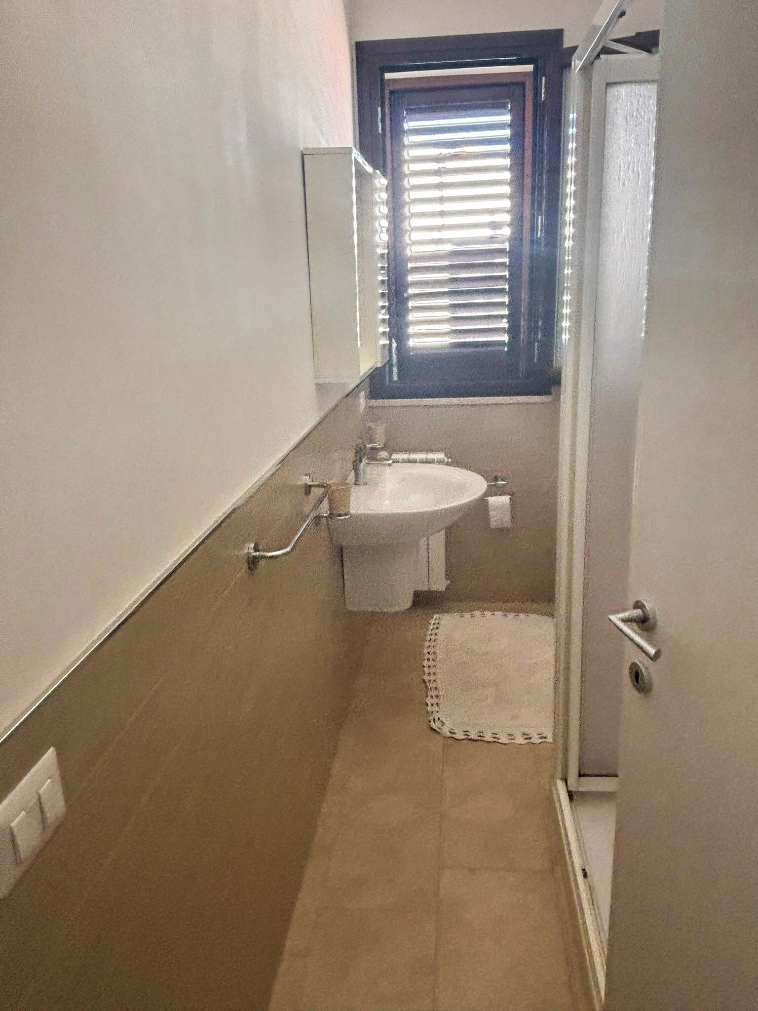 A small bathroom with a toilet, sink, and window with blinds.