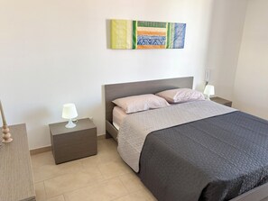 A neatly arranged bedroom with a bed, two bedside tables, and a wall-mounted artwork. - Sofia Kite Apartment (Marsala)