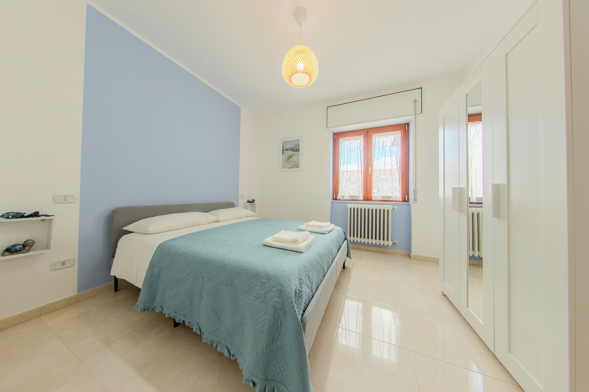 A bedroom with a bed, a radiator, a wardrobe, and a hanging light fixture.