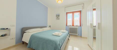 A bedroom with a bed, a radiator, a wardrobe, and a hanging light fixture.