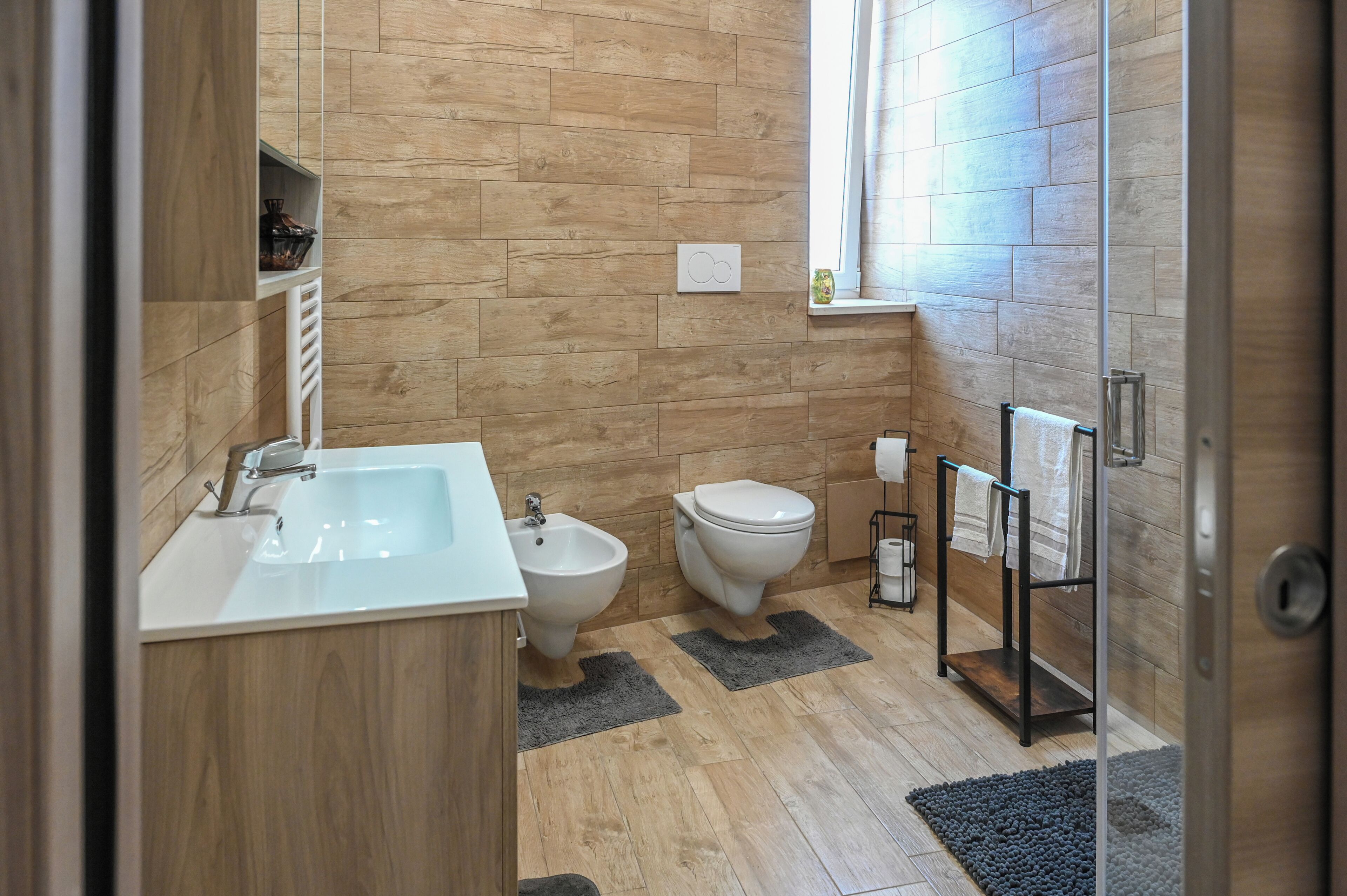 Un baño con suelo de madera, un lavabo blanco, un bidé, un inodoro y un perchero para toallas.