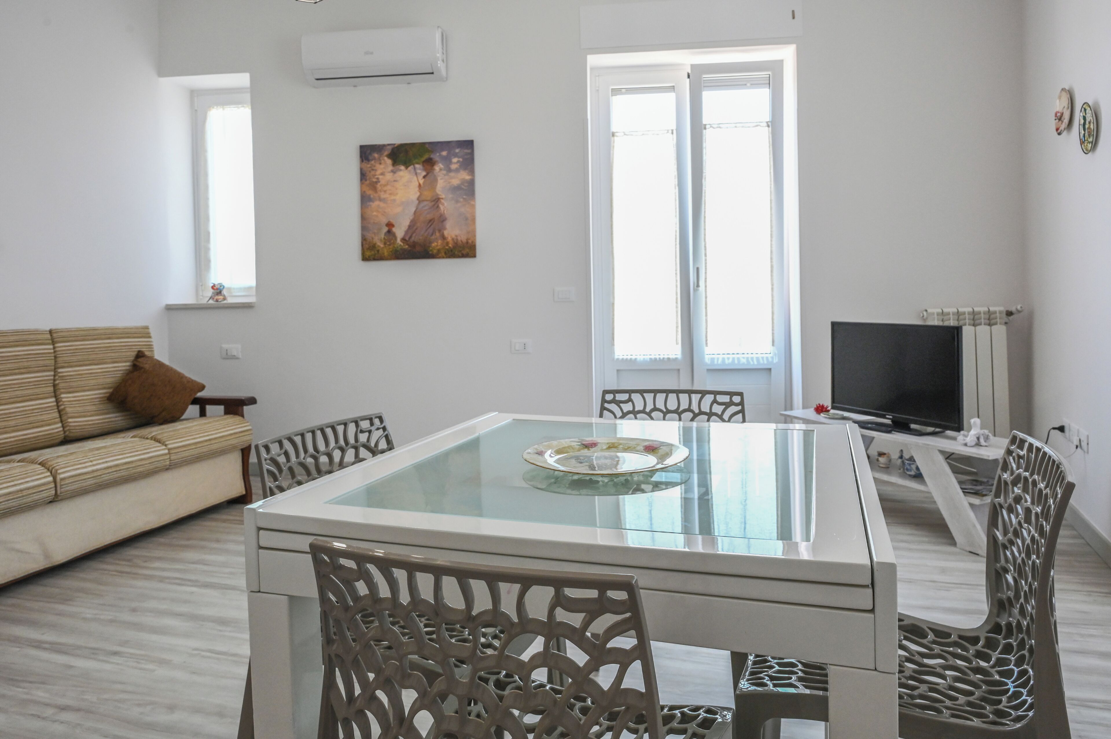 A modern living room with a glass-top dining table, a sofa, and a TV.