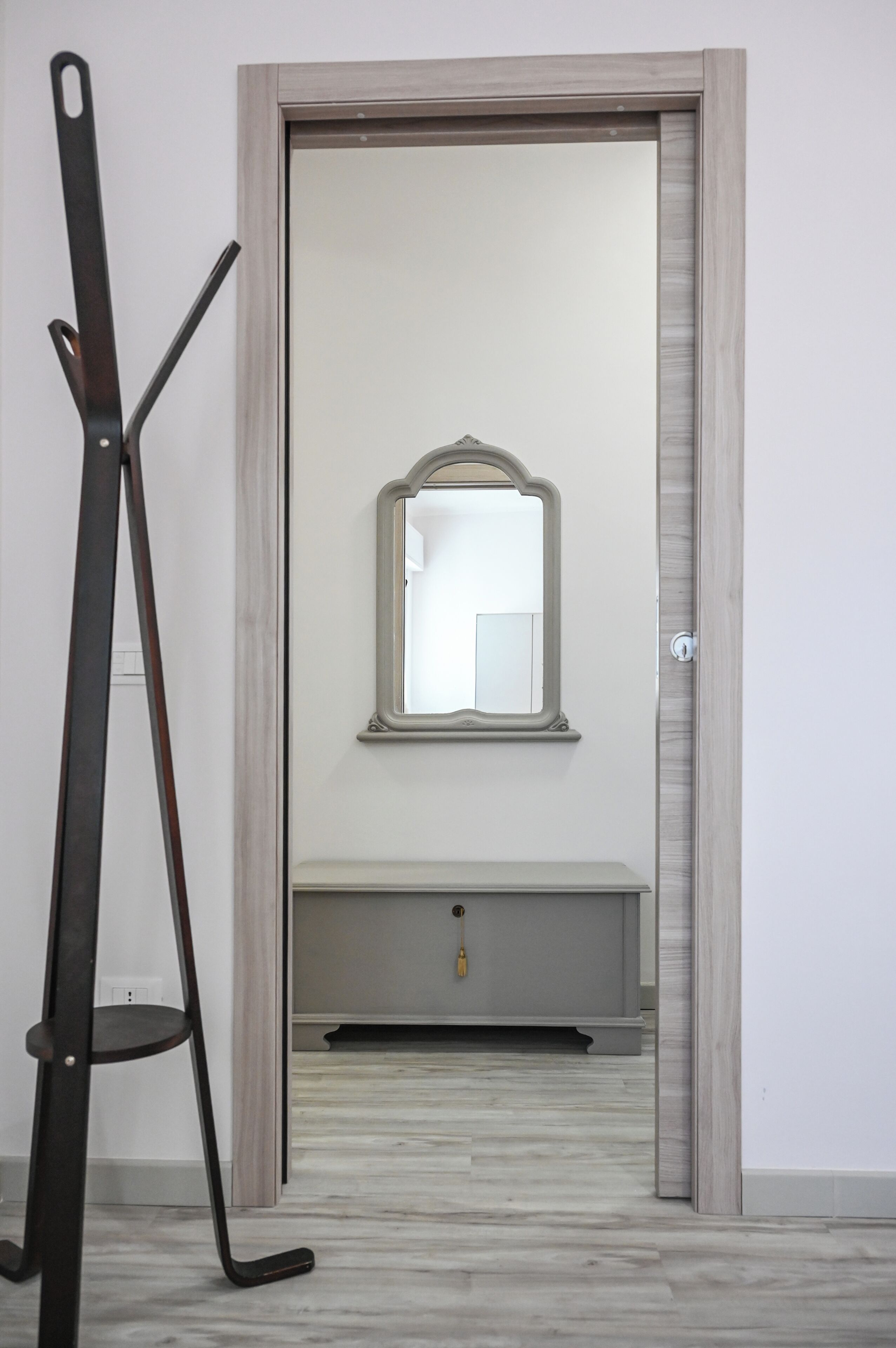A room with a door leading to a bathroom, a mirror on the wall, and a metal stand.