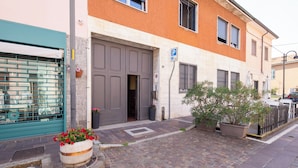 Une vue de rue avec un bâtiment doté d’une grande porte de garage, d’un panneau de signalisation indiquant un espace de stationnement et de plantes en pot.