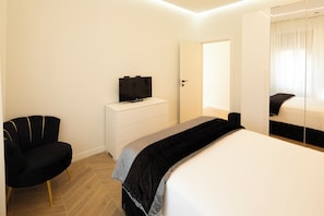 Une chambre à coucher moderne avec un lit, un téléviseur posé sur une commode, une chaise et un grand miroir.