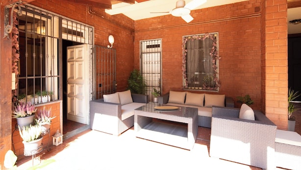 Un espace patio aménagé avec des meubles en osier, un ventilateur de plafond et des plantes en pot.