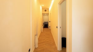 Un couloir étroit avec un parquet en point de Hongrie, des murs blancs et une porte au fond.