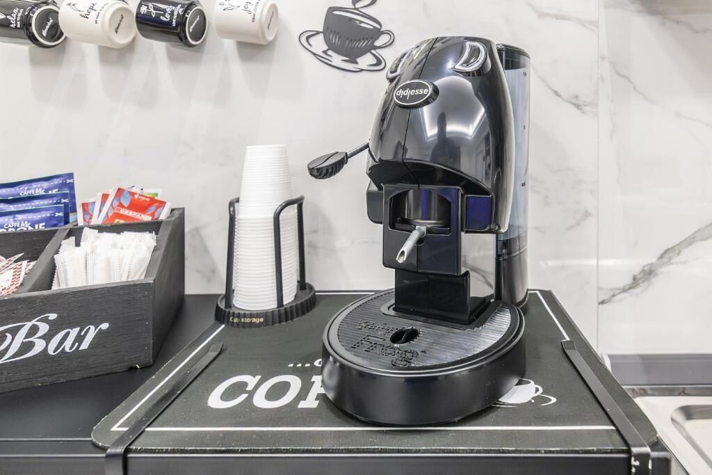 A coffee machine on a counter with a 'Bar' sign, coffee cups, and a storage box.