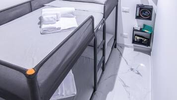 Habitación de hotel con una cama, una mesita de noche con lámpara y una estantería en la pared con un reloj y un marco de fotos.