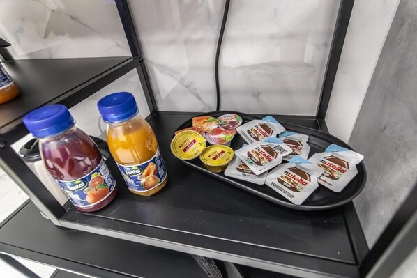 A tray with various food items including jars of jam, a bottle of honey, and packets of Nutella. - Amour (Rosolini)