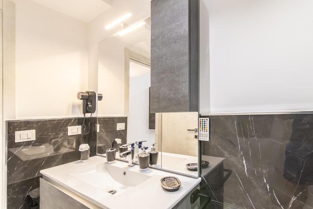 A modern bathroom with a large mirror, a white sink, and a black marble backsplash.