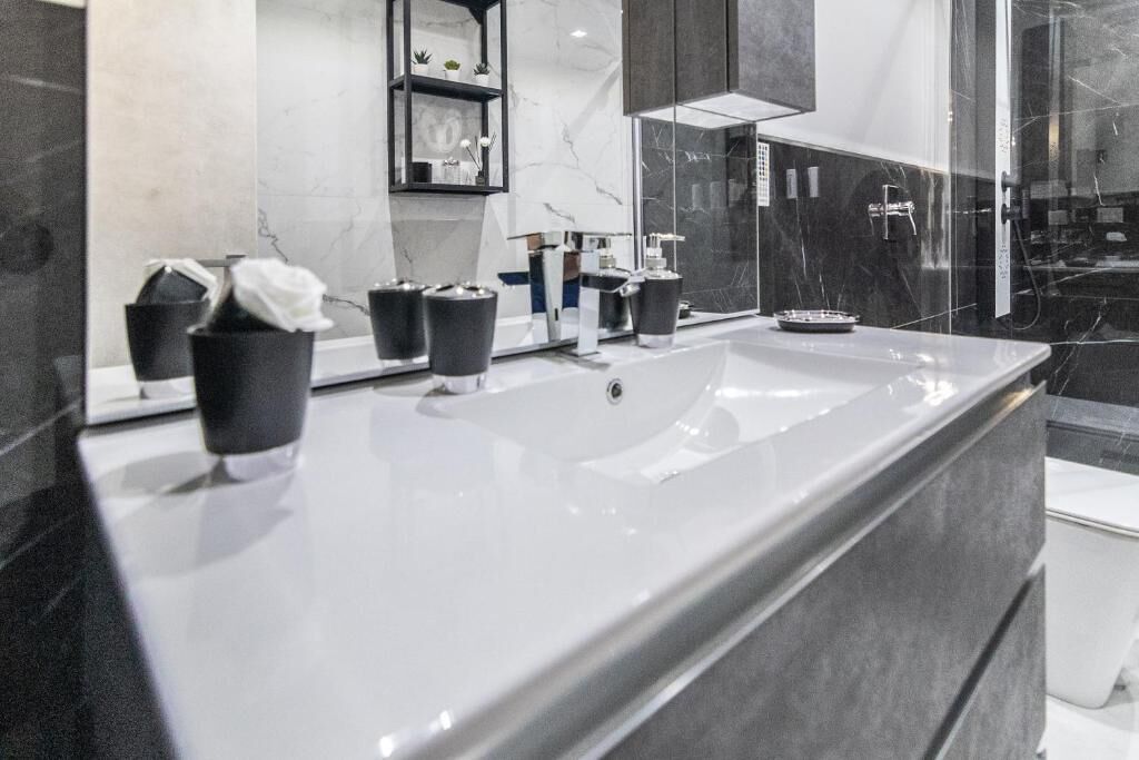 Une salle de bain moderne avec un grand lavabo blanc, des accessoires noirs et un pare-baignoire en marbre.