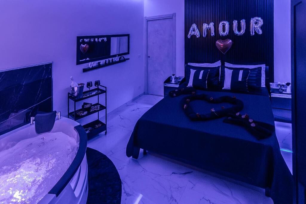 Een slaapkamer met een groot bed, een badkuip en een muur versierd met 'AMOUR' en hartjes.